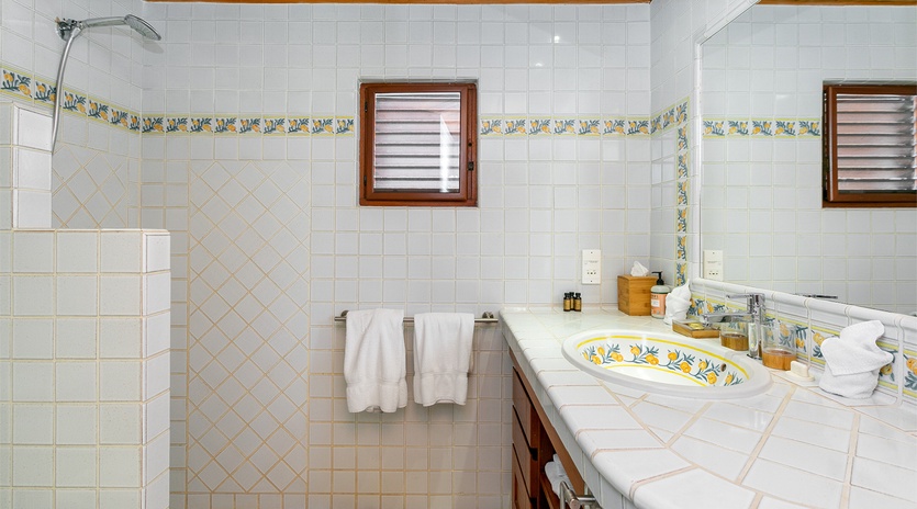 Relax in your bright, spacious bathroom featuring charming Mediterranean-inspired tilework, walk-in shower, handcrafted painted sink, and warm wood ceiling accents that create a welcoming retreat.
