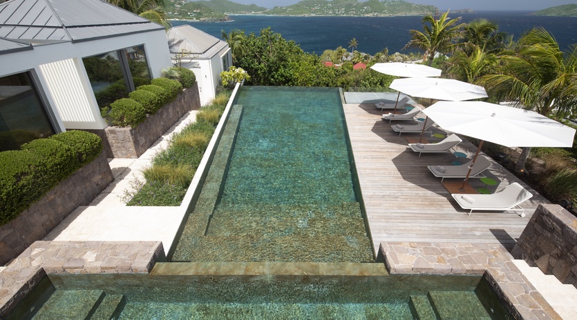 Stunning infinity pool overlooking turquoise Caribbean waters, surrounded by tropical palms and mountains.