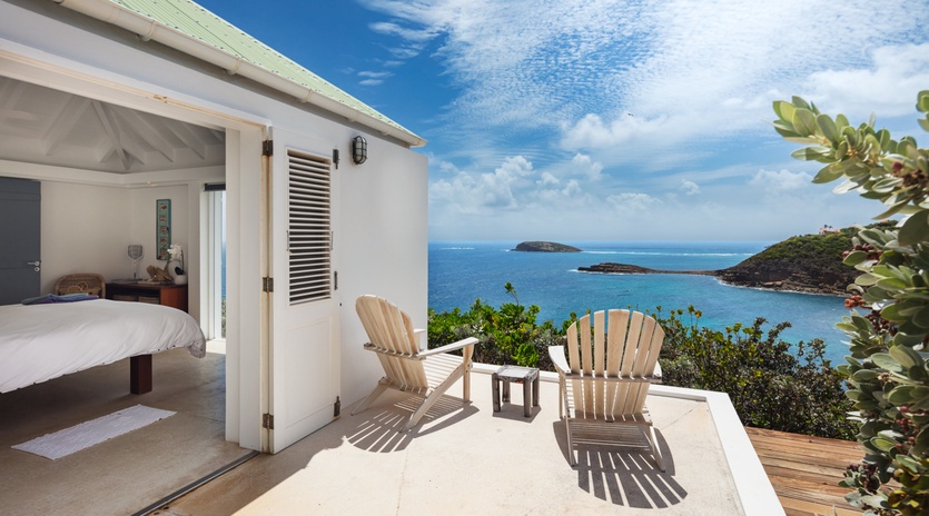 Step onto your private terrace where wooden chairs frame endless blue ocean vistas and distant islands—a serene outdoor retreat just beyond your bedroom door.