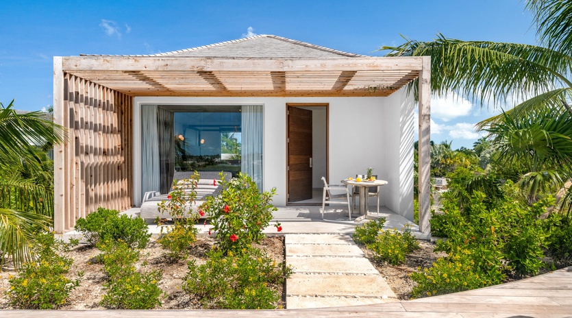 Modern tropical villa with pergola and private terrace surrounded by lush landscaping and palm trees.