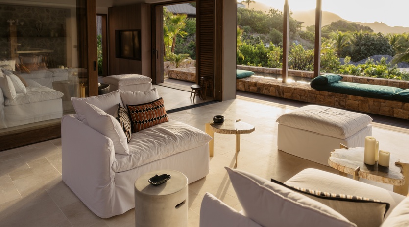 Sink into plush seating while golden light streams through floor-to-ceiling windows, framing lush tropical views from your serene living space.