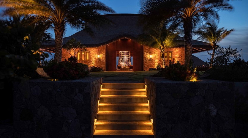 Stone villa with illuminated entrance stairs and tropical palms creates a stunning arrival under twilight skies.