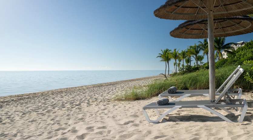 Private beach with lounge chairs and umbrellas, surrounded by swaying palm trees and pristine sand.