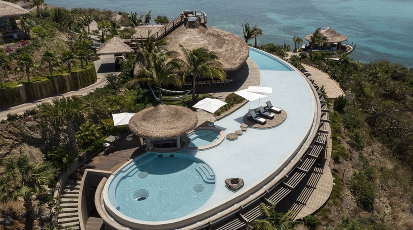 Stunning beachfront resort featuring an infinity pool with swim-up bar, surrounded by tropical palms and crystal-clear ocean views.