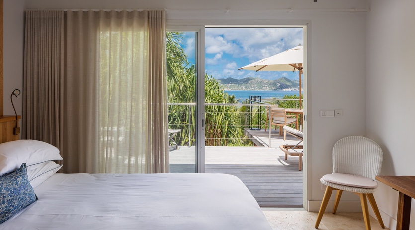 Step into your serene bedroom where crisp white linens meet stunning sea views, and the private balcony invites you to unwind with gentle island breezes and endless blue horizons.