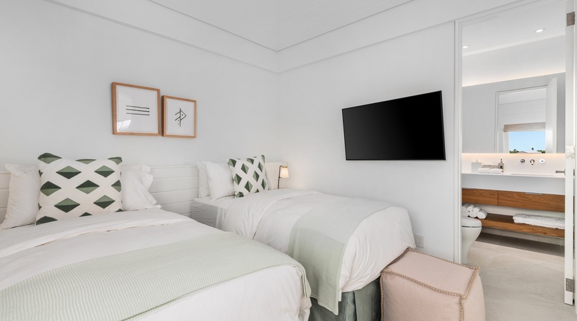 Unwind in your pristine twin bedroom featuring crisp linens, modern amenities, and an elegant ensuite bathroom for ultimate comfort.