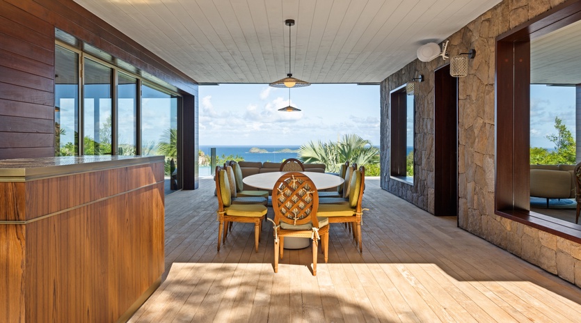 Dine in tropical elegance with ocean views through floor-to-ceiling windows, surrounded by natural stone and warm wood.