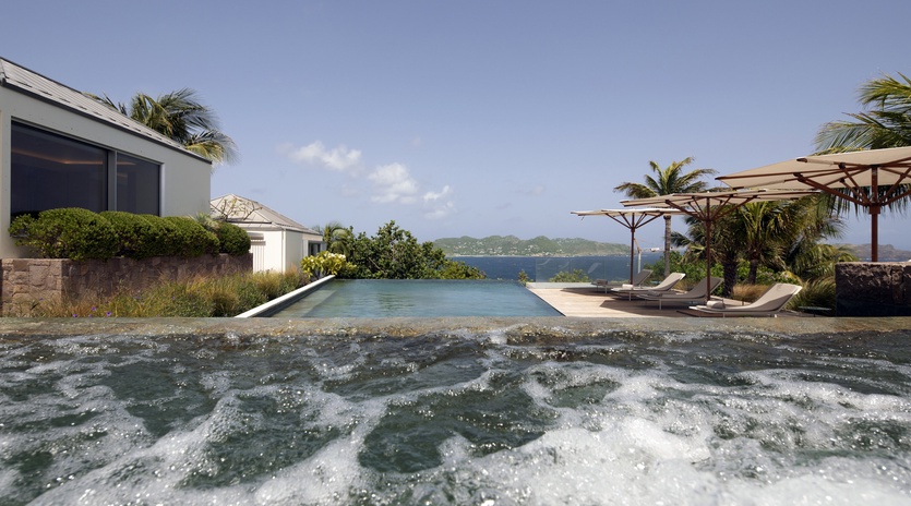 Modern villa with infinity pool overlooking tropical waters, complete with loungers and umbrellas for the ultimate escape.