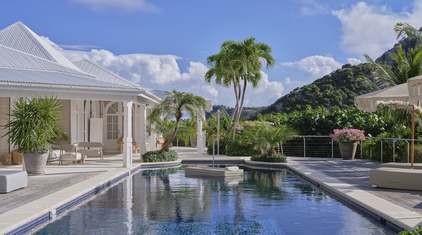 Elegant white villa with pristine pool nestled among tropical palms and lush hillsides under Caribbean blue skies.