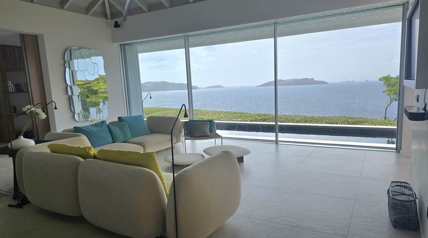 Step into your bright living room where floor-to-ceiling windows frame endless ocean views. Sink into plush seating and let the tranquil blues wash over you—this is your Caribbean escape.