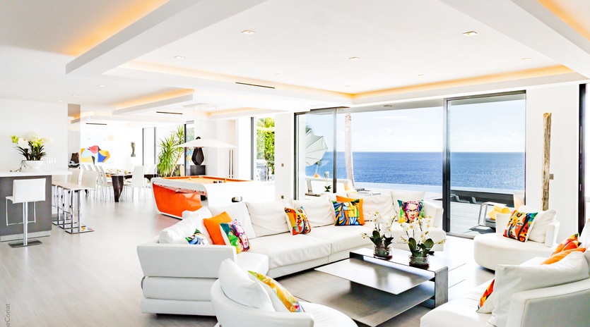 Sink into plush white sofas while soaking up endless ocean views through floor-to-ceiling windows in this bright, modern living space.