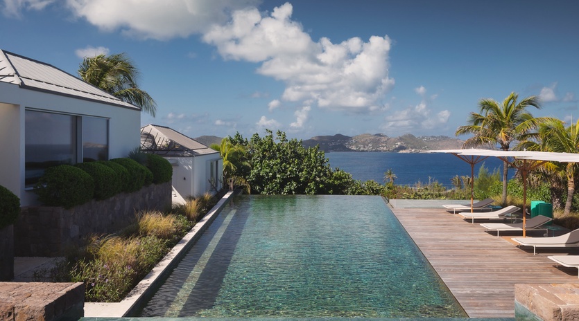 Modern villa featuring infinity pool with panoramic ocean views across tropical waters to distant mountains.