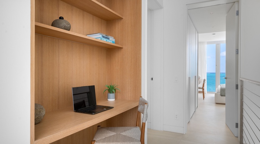 Your dedicated workspace features warm wood built-ins with a view of the sparkling ocean beyond.
