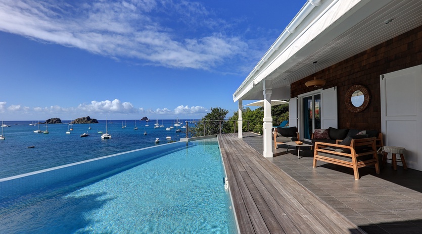 Stunning infinity pool overlooking crystal-clear Caribbean waters with boats dotting the horizon. Modern tropical paradise.