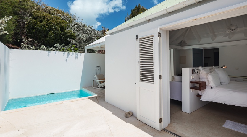 Step from your cozy bedroom directly onto a sunny terrace where a private plunge pool awaits—an intimate oasis framed by whitewashed walls, loungers, and blue skies overhead.