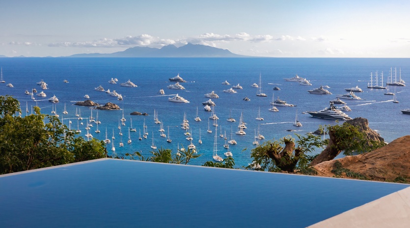 Infinity pool overlooking pristine harbor with luxury yachts and distant mountain vistas.