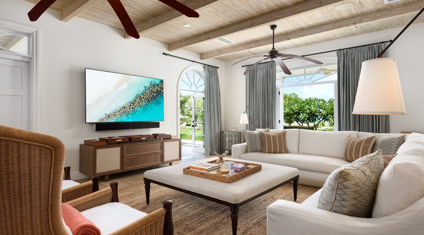 Relax in your spacious living room with vaulted ceilings, cozy seating, and stunning views of lush tropical greenery just beyond the glass doors.