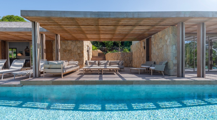 Modern villa featuring a stunning infinity pool and covered outdoor lounge area with natural stone walls.
