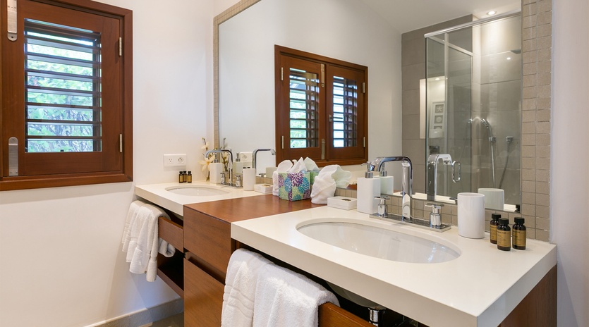 Unwind in your serene bathroom with dual vanities, a walk-in shower, and natural light through tropical shutters—your private spa awaits.