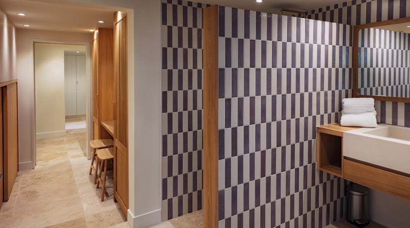Modern spa changing area with geometric tiled walls, warm wood accents, and fresh towels ready for your wellness retreat.