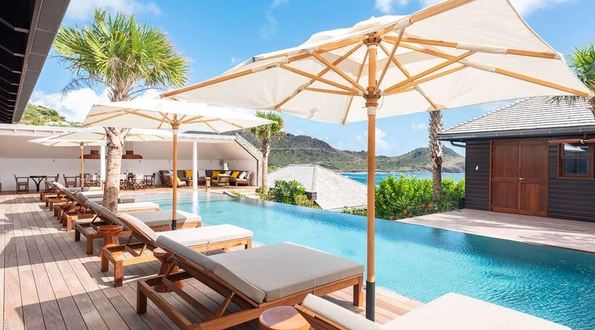 An infinity pool overlooking turquoise waters and lush mountains, with plush loungers beneath elegant umbrellas inviting you to unwind in pure paradise.