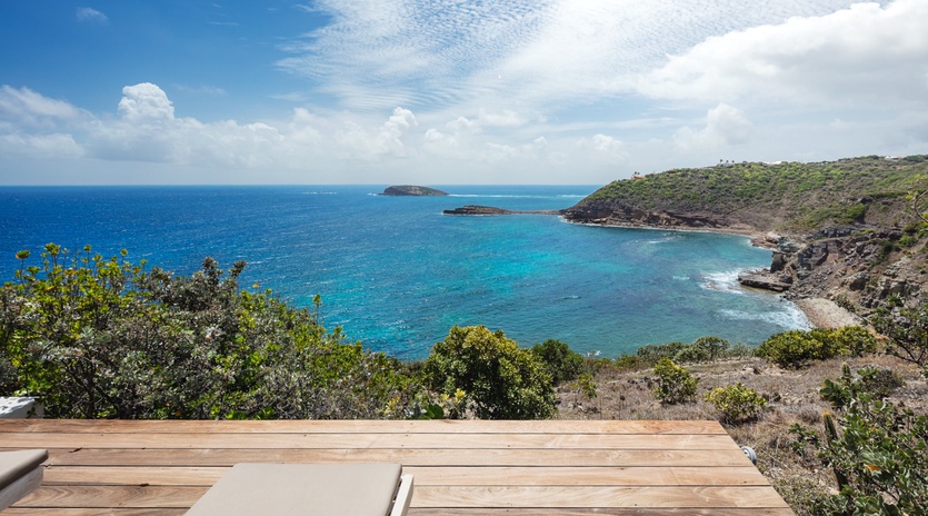 Stunning coastal panorama with turquoise waters, volcanic cliffs, and lush green hills overlooking a secluded bay. A tranquil escape near pristine beaches.