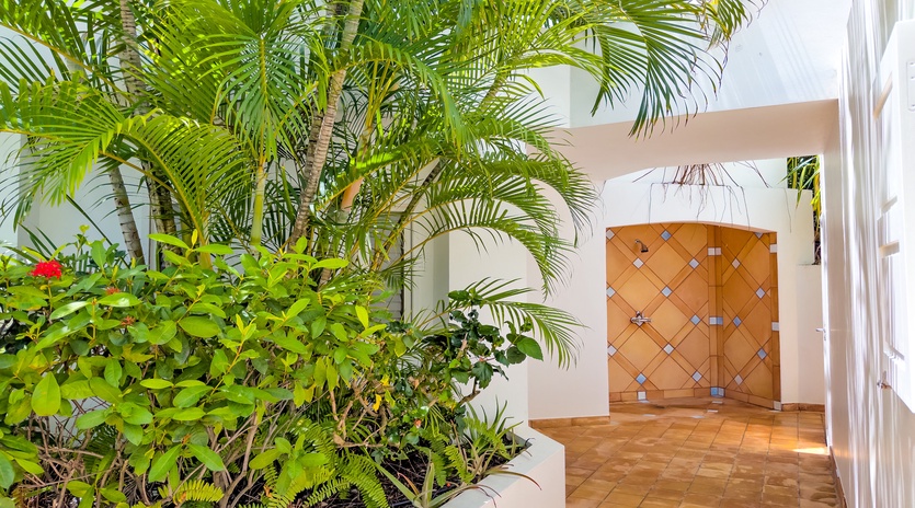 This distinctive entrance features tropical landscaping with lush palms and vibrant plantings surrounding a decorative tiled archway, welcoming guests to the property with island charm.