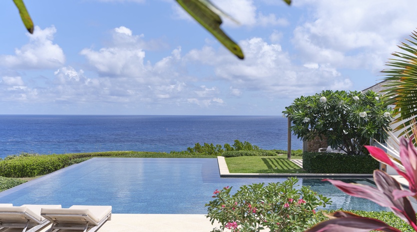 An infinity pool nestled within manicured tropical gardens, with the sparkling blue ocean stretching endlessly beyond. Perfect for soaking up paradise in total serenity.