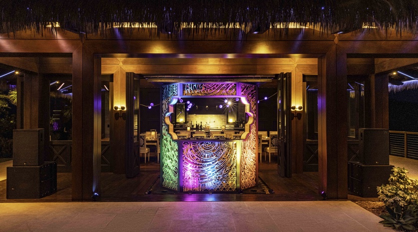 Stunning thatched-roof bar and lounge with vibrant lighting creates an exotic tropical atmosphere for evening relaxation.