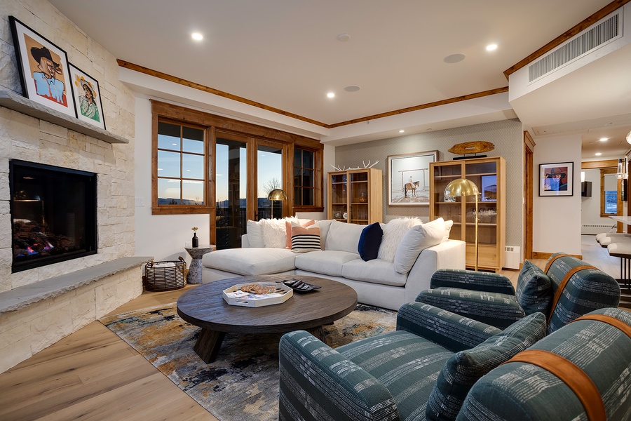 Sink into plush seating by the stone fireplace, where warm wood tones and soft lighting create your perfect evening retreat. Scenic windows frame stunning views, inviting you to unwind in comfort.