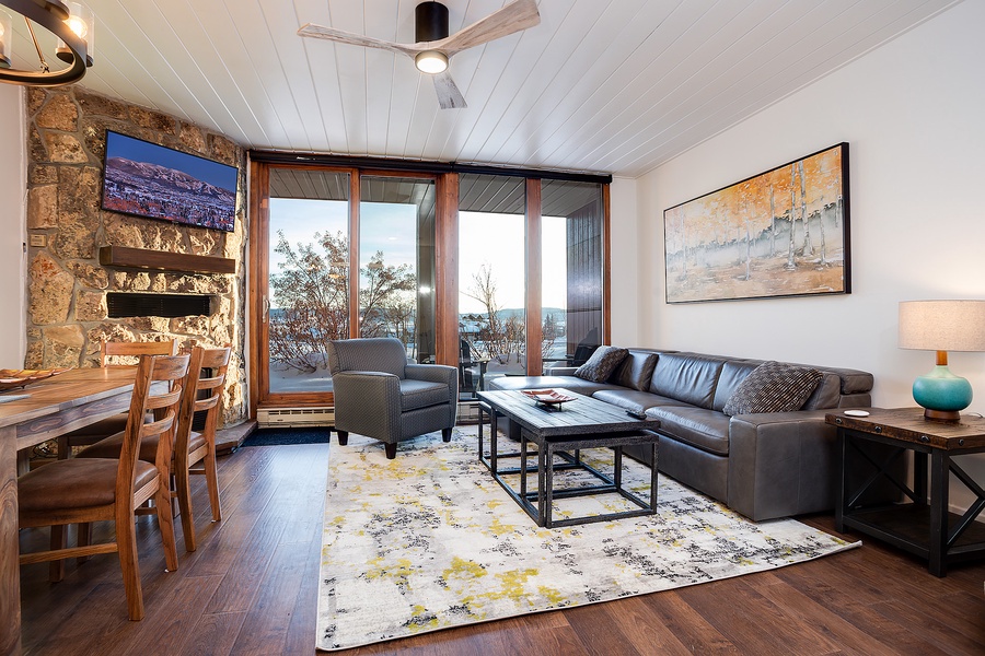 Relax in your open-concept living space with soaring ceilings, a cozy stone fireplace, and large glass doors framing stunning mountain views—your perfect retreat after a day of adventure.