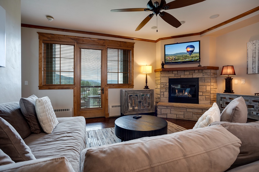 Unwind in your spacious living room with a crackling stone fireplace, plush seating, and serene mountain views through the balcony doors—your perfect retreat after adventure.