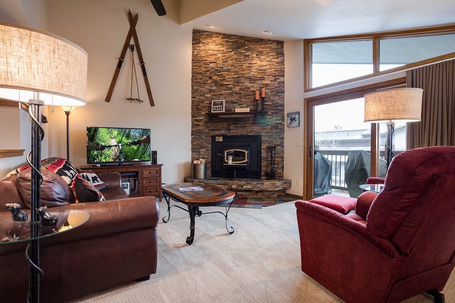 Unwind in this inviting living space with plush seating, a cozy stone fireplace, and large windows framing mountain views—your perfect retreat after a day of adventure.