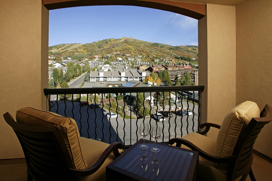 Balcony overlooking a scenic mountain landscape with colorful autumn foliage, neighboring buildings, and charming village nestled in the hillside. Comfortable seating awaits your morning coffee or evening relaxation.