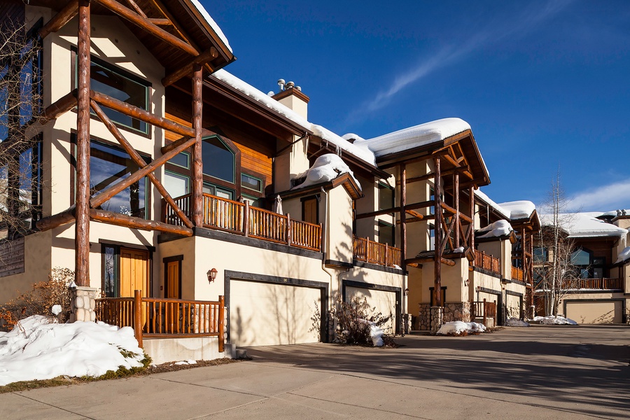 Charming mountain townhomes with rustic timber accents and private balconies, nestled in a peaceful winter setting under bright blue skies.