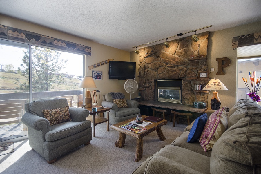 Unwind in your cozy living room with a crackling fireplace, plush seating, and warm mountain views framing the windows—perfect for relaxing after a day of adventure.