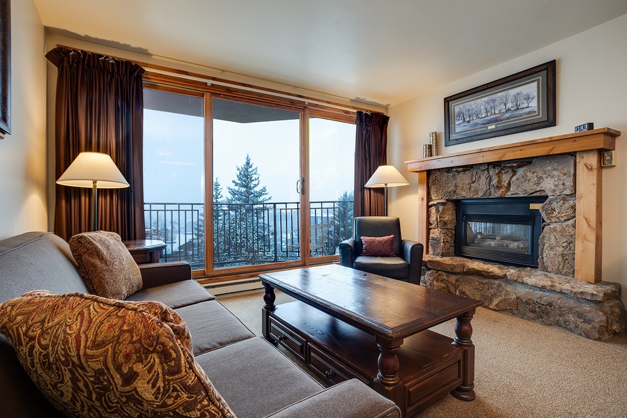Settle into your mountain retreat with a stone fireplace and floor-to-ceiling windows framing stunning alpine views. Cozy up on plush sofas as natural light fills this welcoming living room.