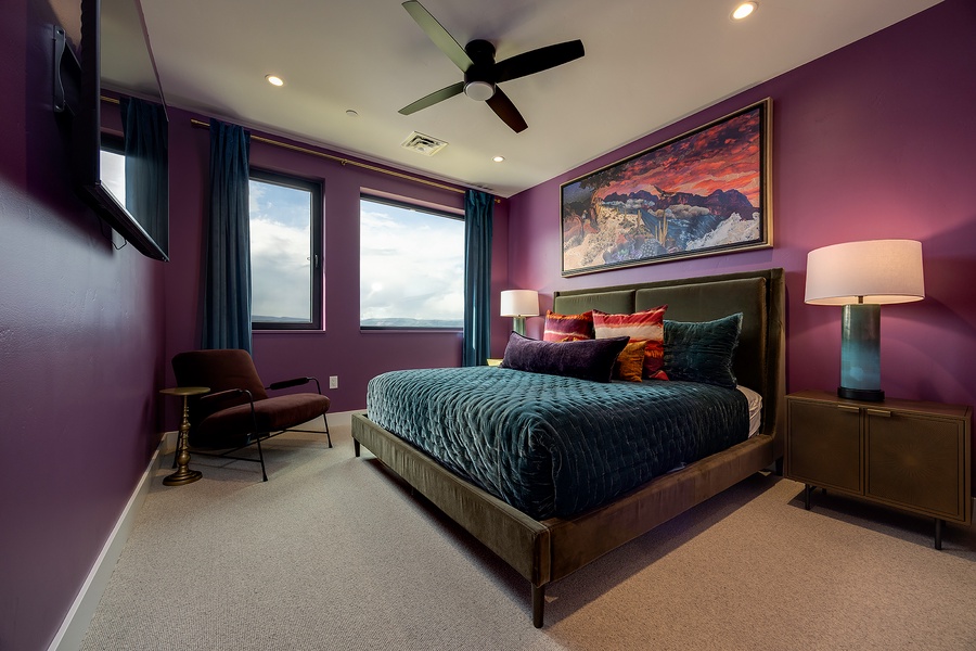 Relax in this thoughtfully designed bedroom with rich purple walls, a ceiling fan, and vibrant decor—your perfect retreat after a day of adventure.