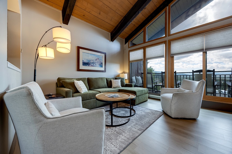 Sink into comfortable seating in your bright, open living room, where soaring wood-beamed ceilings and floor-to-ceiling windows frame stunning mountain views from your private balcony.