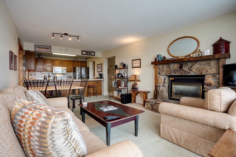 Relax in your spacious open-concept living area featuring a cozy stone fireplace, comfortable seating, and a fully-equipped kitchen ready for your mountain getaway meals.