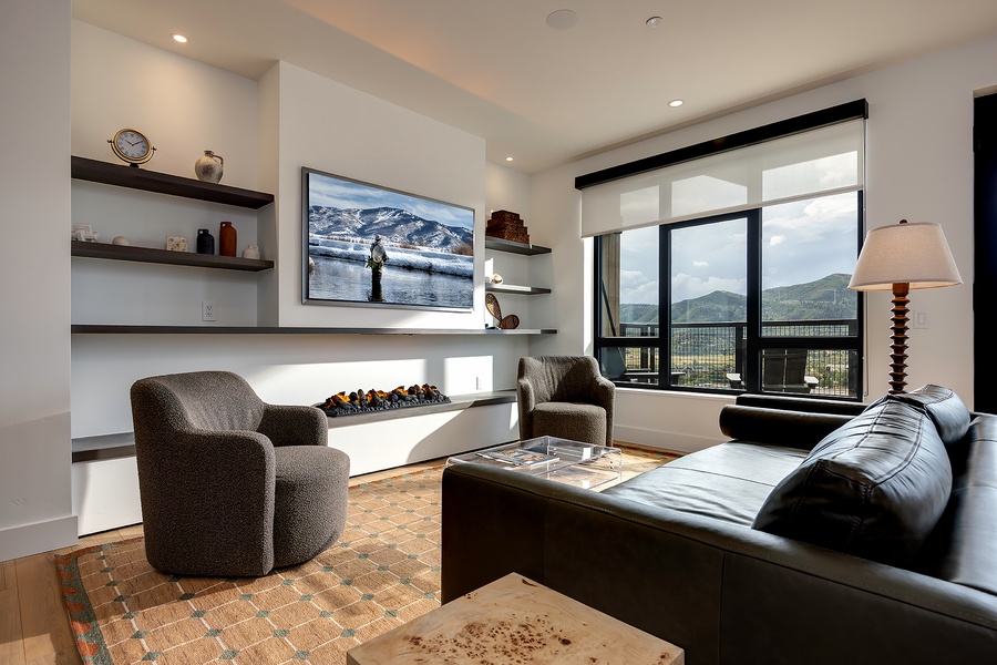 Settle into the plush seating and let your gaze wander to the sweeping mountain vistas framed by expansive windows. The modern fireplace adds warmth, while stylish shelving displays thoughtful touches that make this space feel like home.