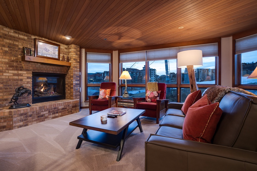 Unwind in your welcoming living space with a crackling fireplace, plush seating, and floor-to-ceiling windows framing stunning mountain vistas—perfect for cozy evenings after a day of adventure.