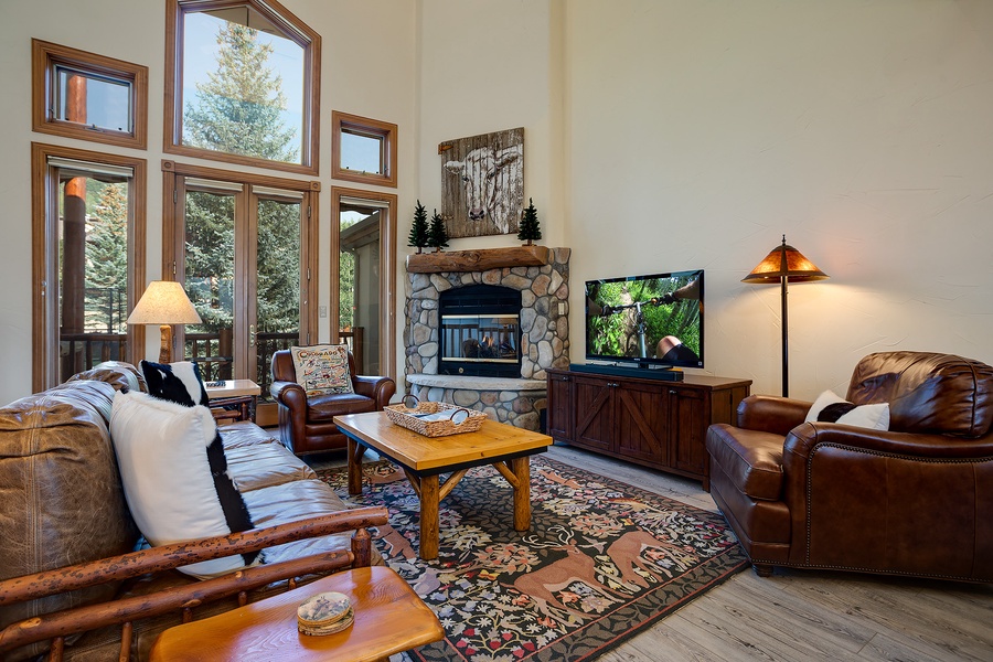Unwind in your cozy living room, where natural light pours through soaring windows, a stone fireplace adds rustic charm, and comfortable furnishings invite you to relax after a day of adventure.