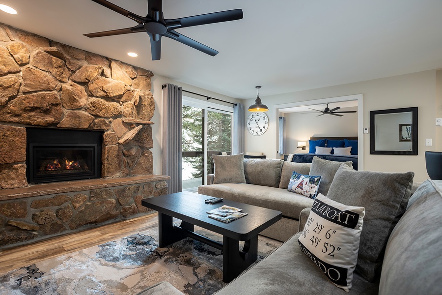Unwind in your inviting living space with a cozy stone fireplace, plush seating, and ceiling fans. The glass doors frame serene views, while the adjacent bedroom beckons for restful nights.
