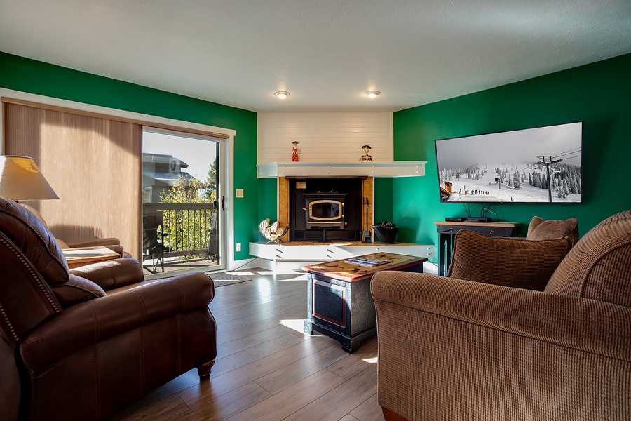 Picture yourself unwinding in this inviting living room, where warm wood tones and bold emerald walls create a cozy alpine retreat. Your balcony opens to scenic views, while the fireplace promises relaxing evenings ahead.
