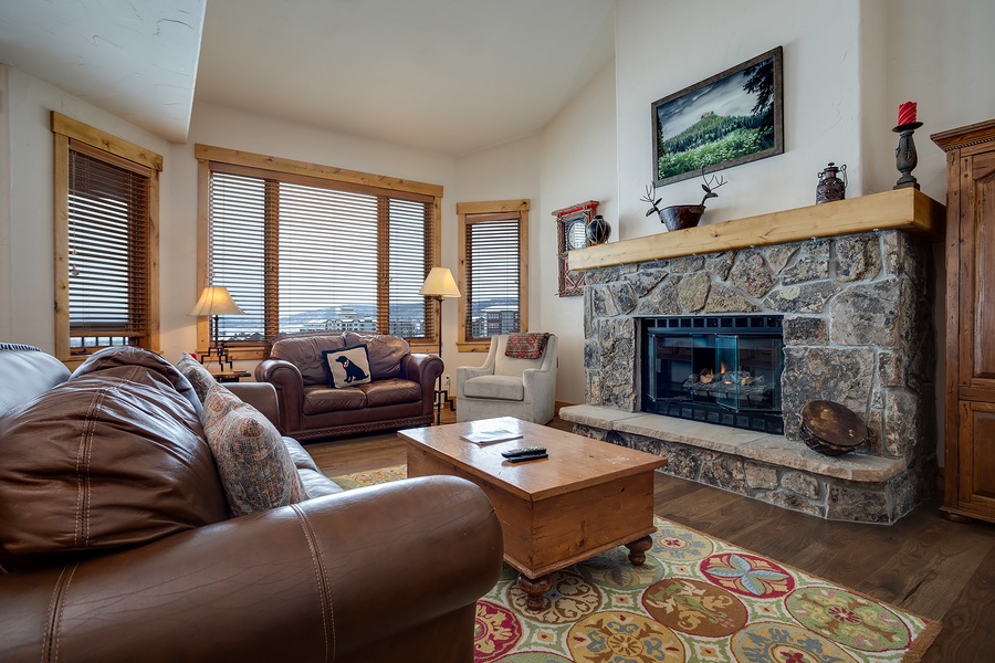 Your inviting living room features a stunning stone fireplace, plush leather seating, and mountain views through expansive windows—perfect for unwinding after a day exploring nearby trails.