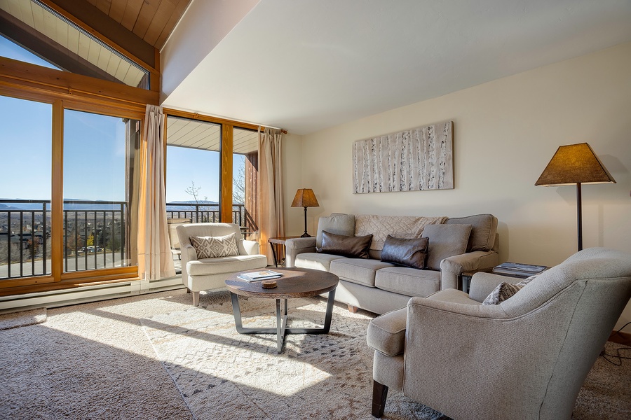Sink into plush seating as natural light fills your living room, where vaulted ceilings and panoramic balcony views create your perfect mountain retreat.