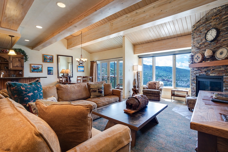 Settle into plush seating surrounded by warm wood beams and a stone fireplace while soaking in stunning mountain views through floor-to-ceiling windows. Your perfect mountain retreat awaits.