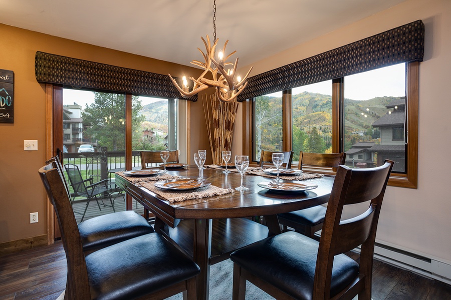 Gather around this warm dining space where mountain views frame every meal. The rustic antler chandelier and rich wood tones create a cozy mountain retreat feel, perfect for your group dinners and morning coffee.