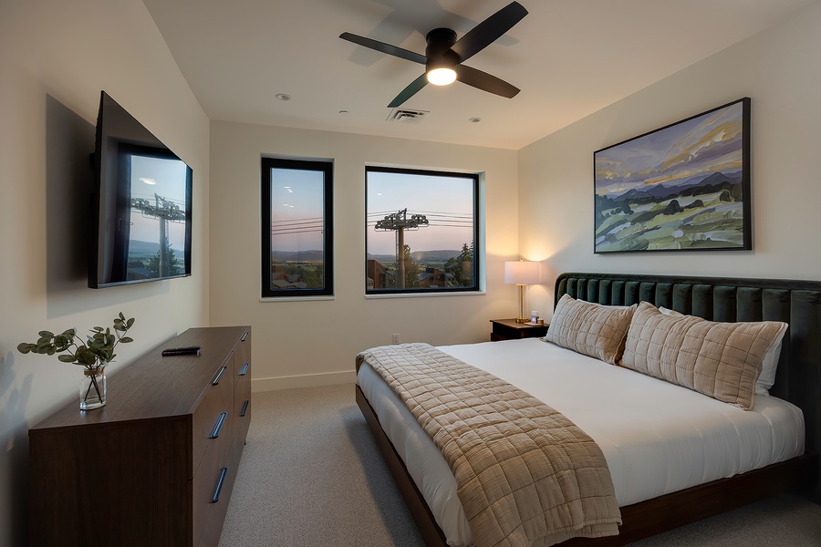Drift off in your serene bedroom with soft linens, modern furnishings, and windows framing peaceful neighborhood views. The ceiling fan keeps you comfortable while artwork and warm lighting create a welcoming retreat.